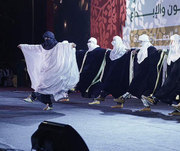 ممثلون بأردية تقليدية ولثام للوجه يرقصون على المسرح.